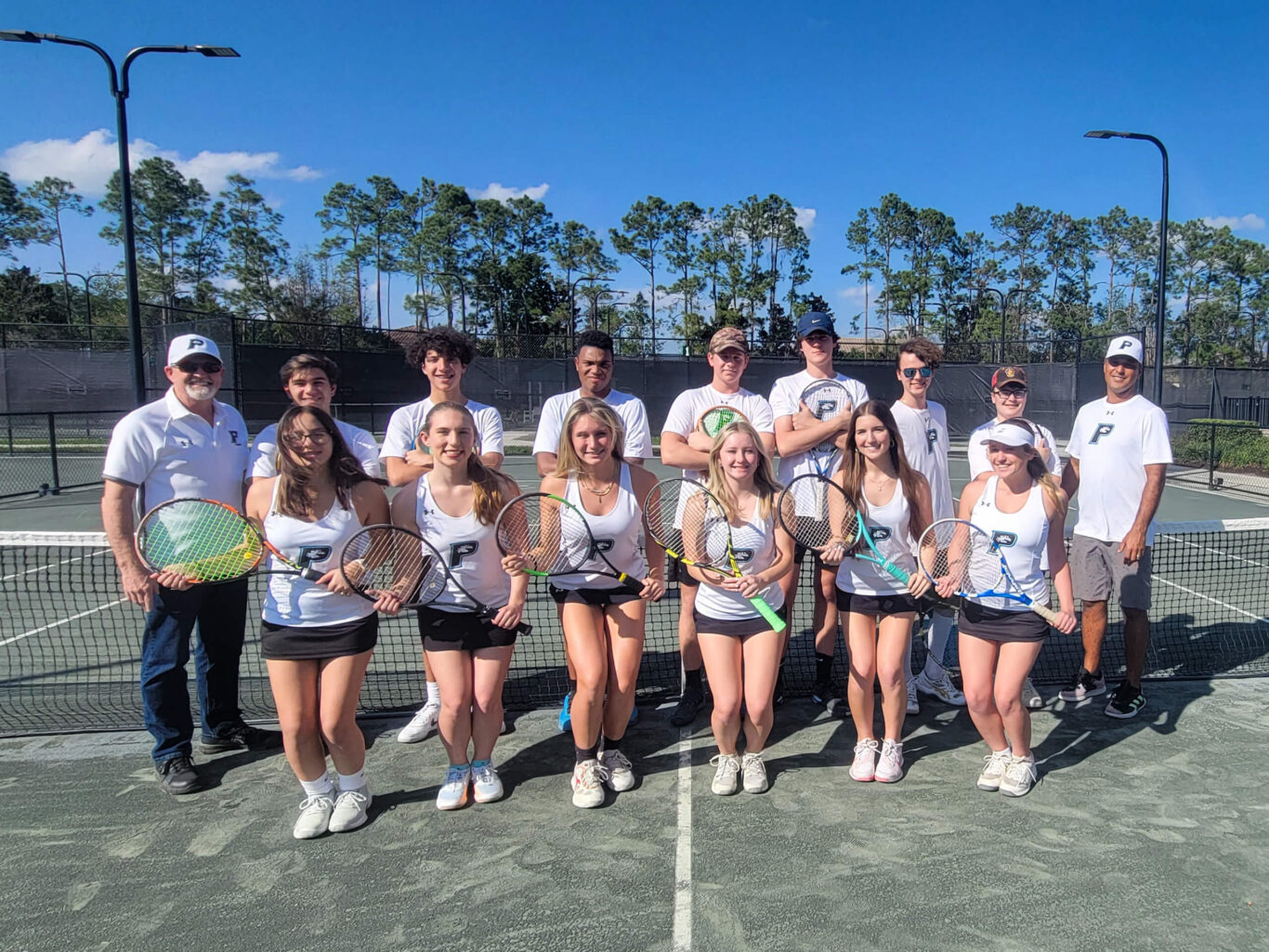 A group of girls posing for a picture on a tennis court.