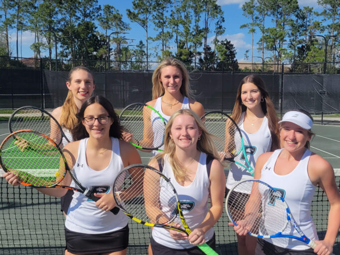 Four female tennis players posing for a picture on a tennis court.