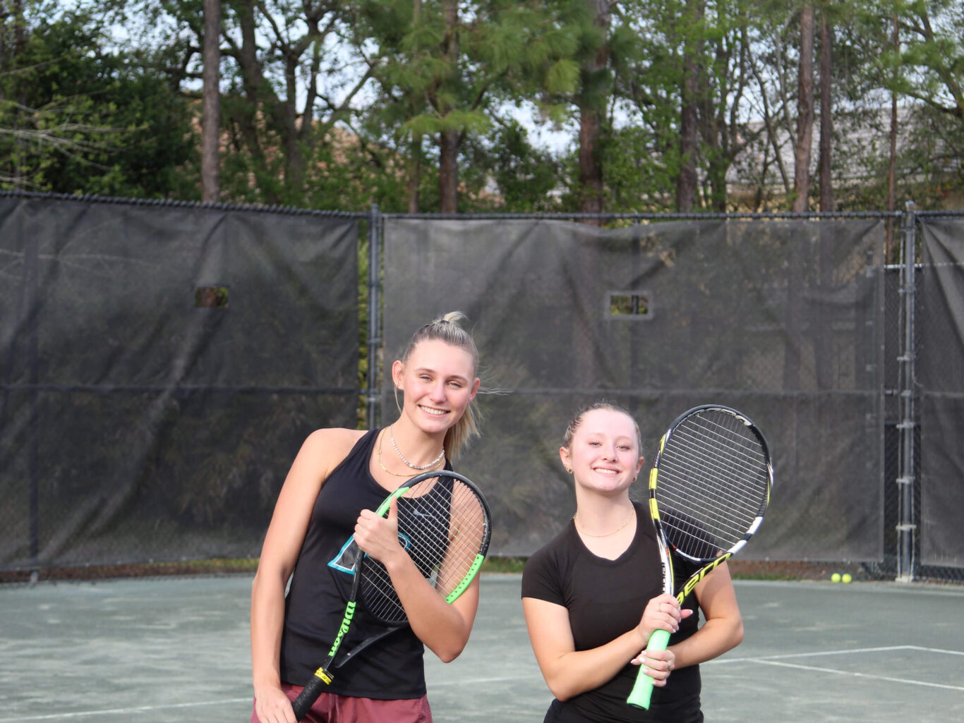 Two girls holding tennis rackets on a tennis court.