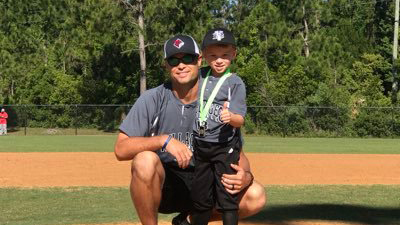 Tommy Boss, the Head Baseball Coach, posing with a young boy on a baseball field.