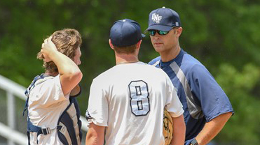 Three baseball players talking to each other on a field while being observed by their Head Baseball Coach, Tommy Boss.