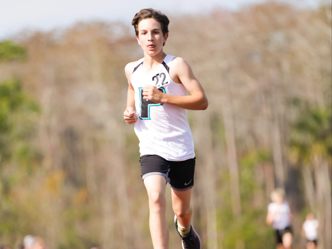 A young man running in a cross country race on a track.