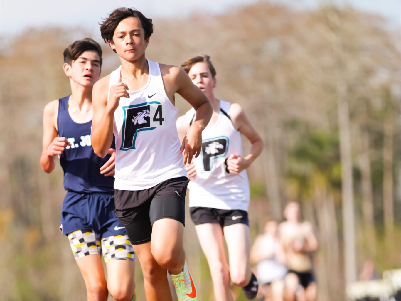 A group of boys running on a track field in a race.