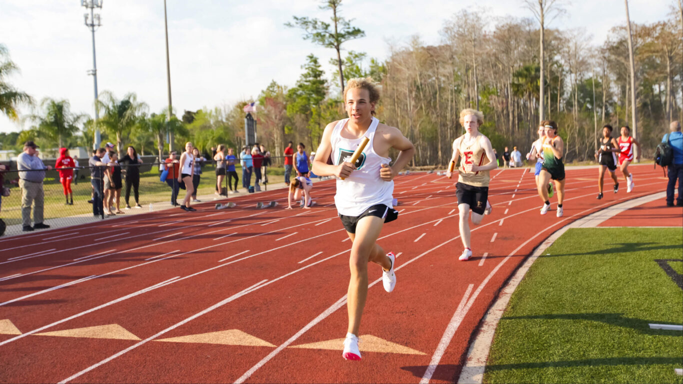 A man running on a track in front of spectators.