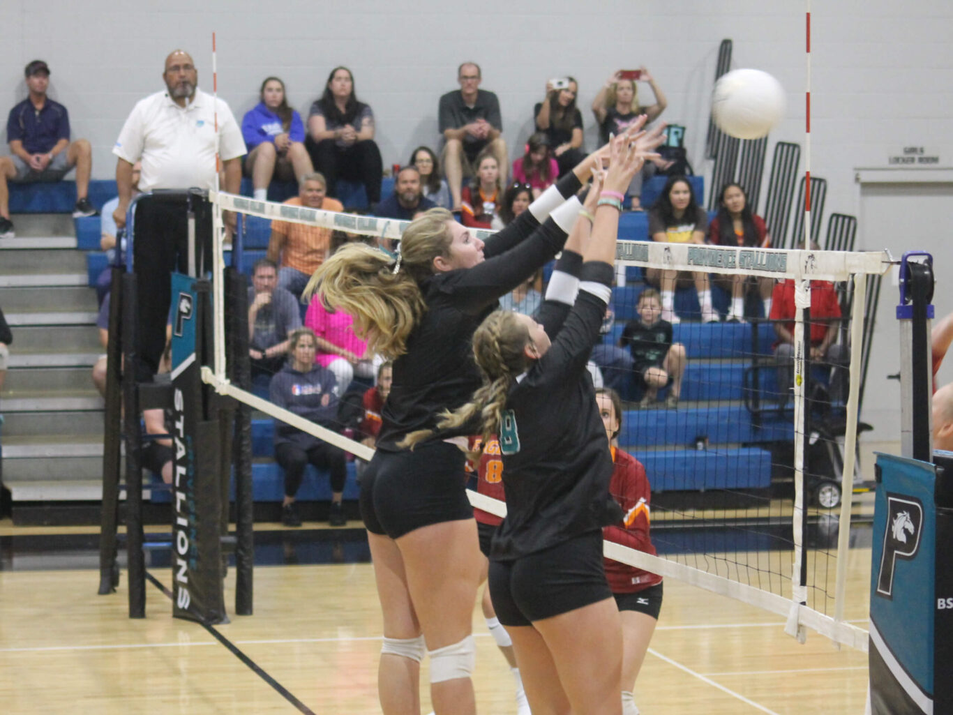 A group of girls playing volleyball and attempting to block the ball.