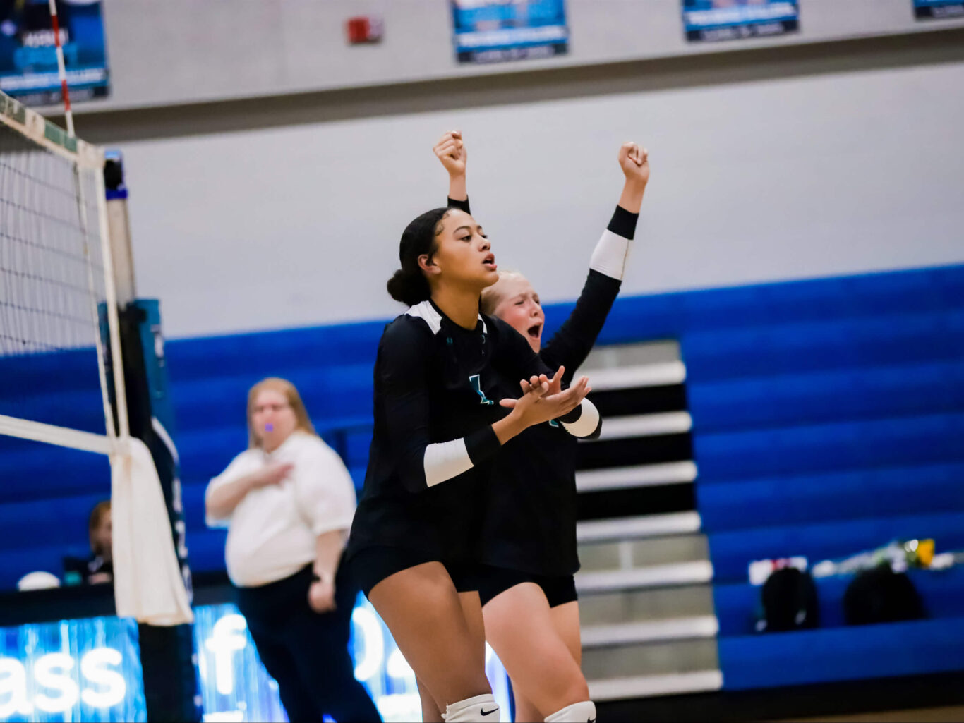 A volleyball player, typically a girl, is raising her arms in the air during a game.