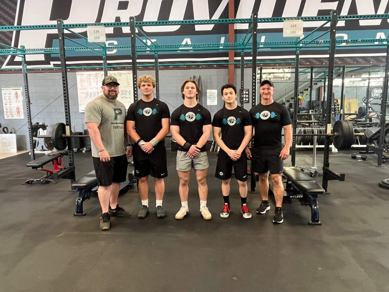 A group of boys posing for a photo in a gym, showcasing their weightlifting skills.