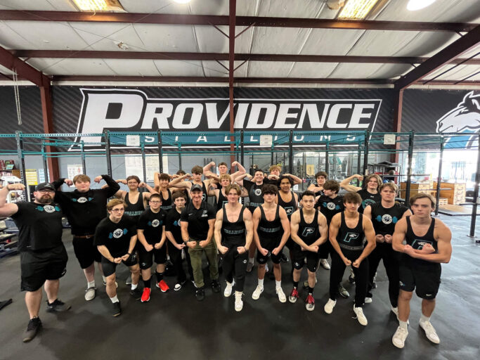 A group of boys posing for a photo in a gym while weightlifting.