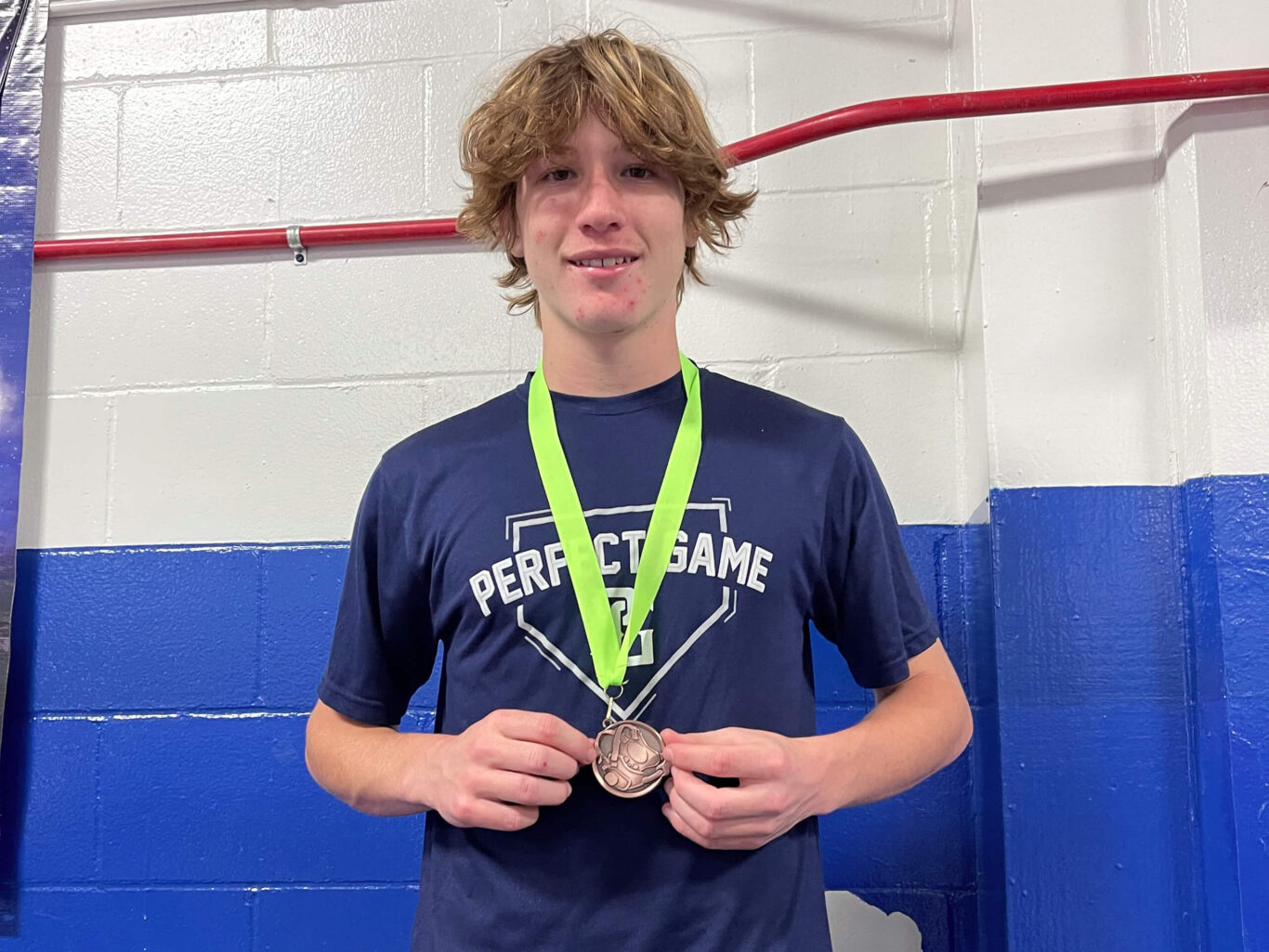 A young man holding a wrestling medal in front of a wall.