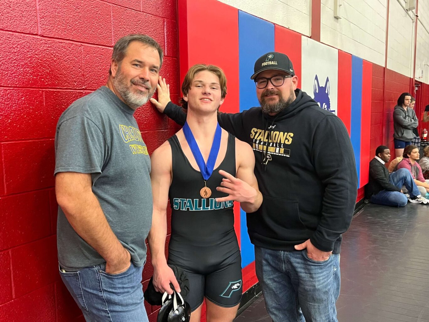 Three boys wrestling with their medals, posing for a picture.